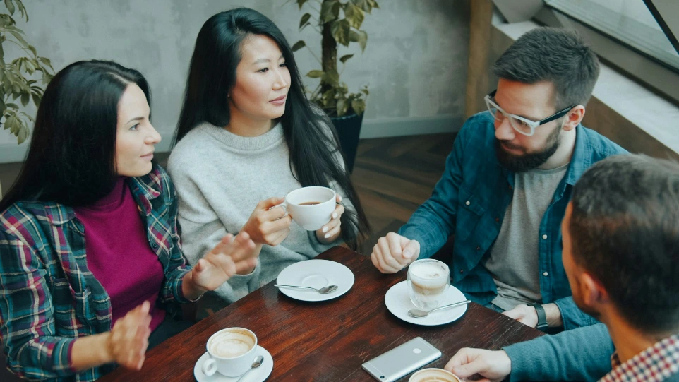 Four people talking while drinking coffee at a wooden table in a cafe